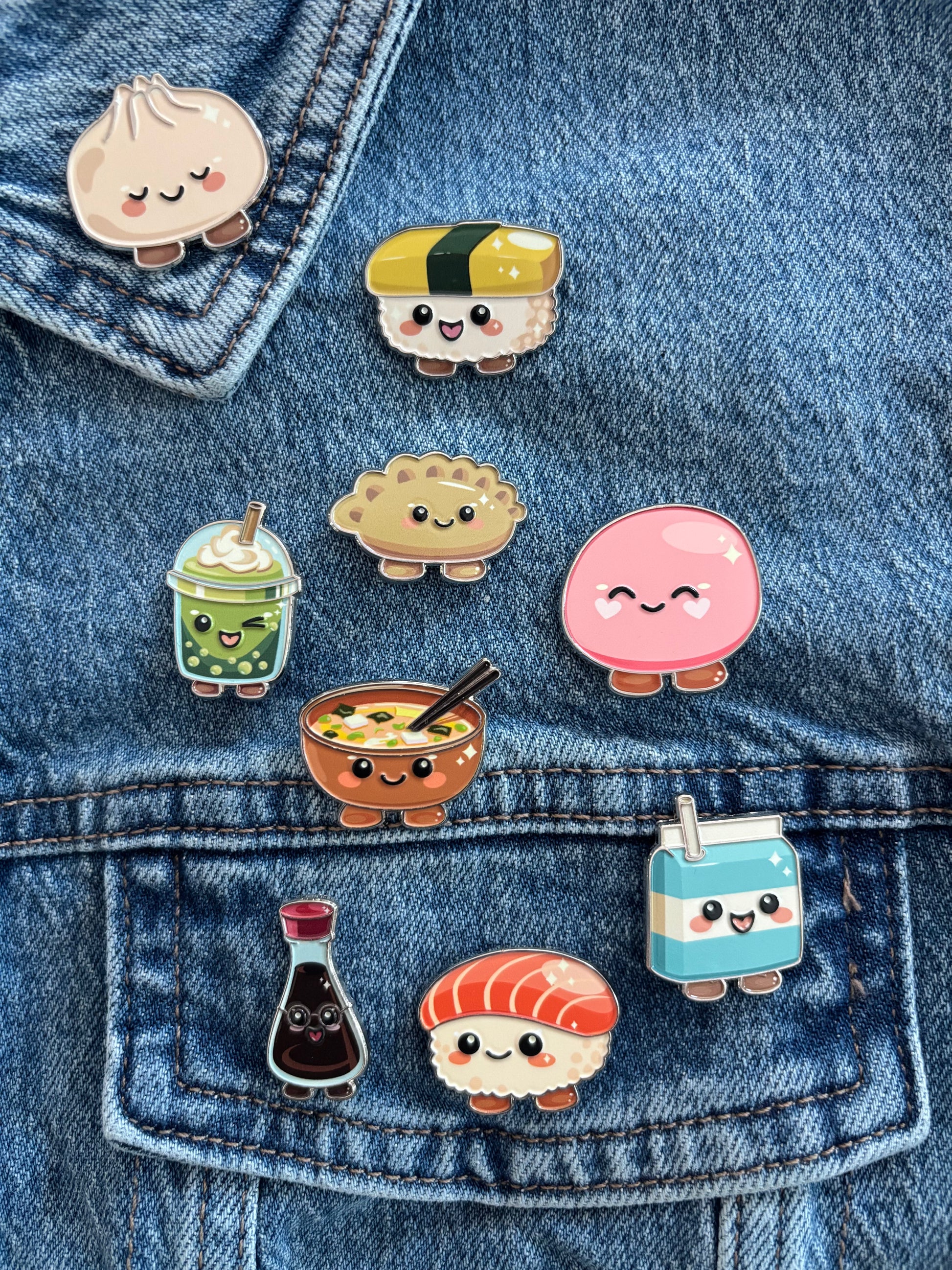Nine cute sushi-themed enamel pins are arranged on a blue denim jacket pocket. The pins feature cartoon characters resembling a kind dumpling, sunny egg maki wrap, bubbly matcha tea, gentle mochi, patient bowl of ramen, smart soy sauce bottle, sweet salmon sushi, cheerful gyoza and a cool milk carton.
Copyright © Cute Bites® All rights reserved.