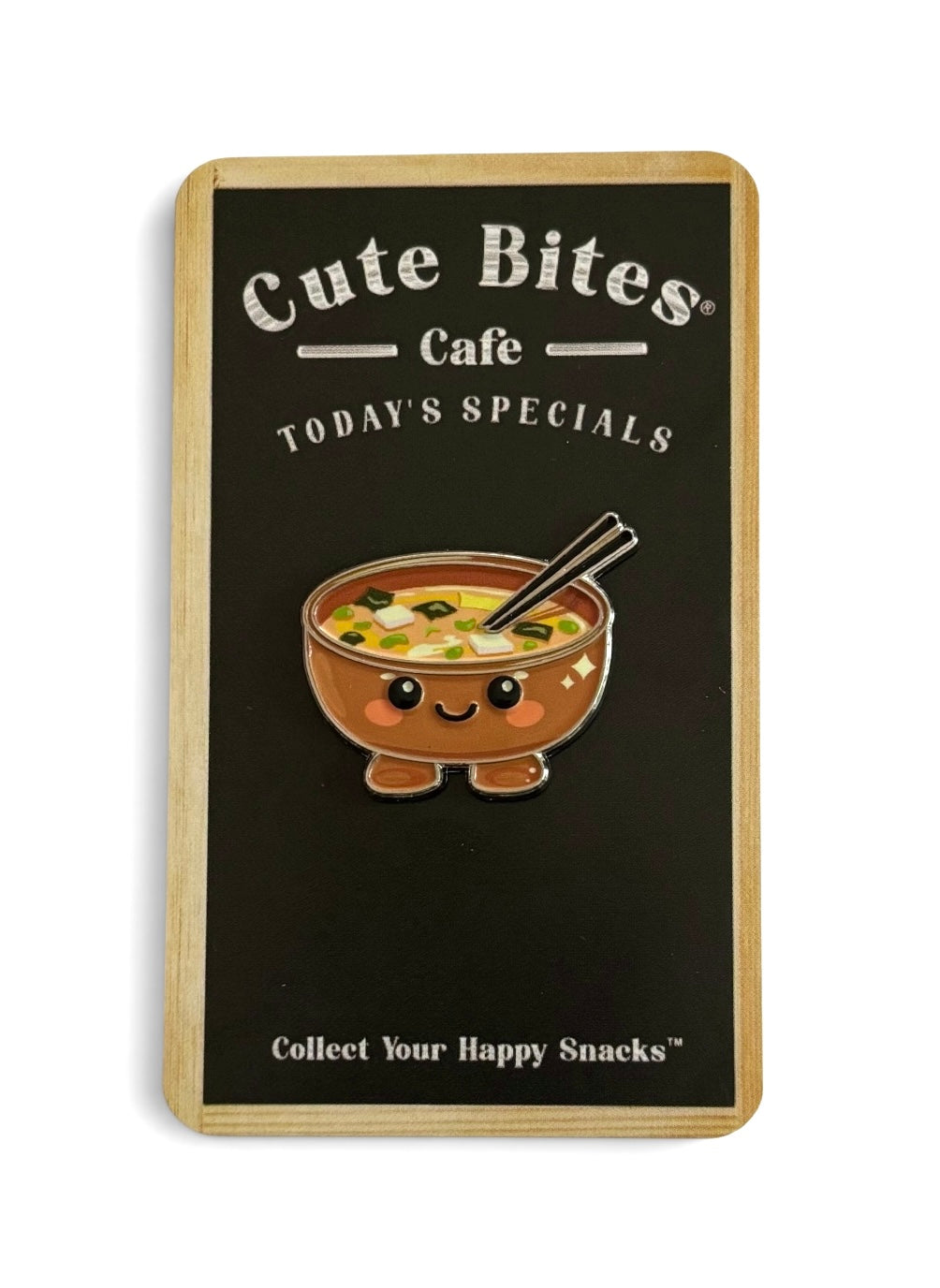 An enamel pin of a smiling bowl of patient ramen with chopsticks. The sign also reads 'Collect Your Happy Snacks' at the bottom.