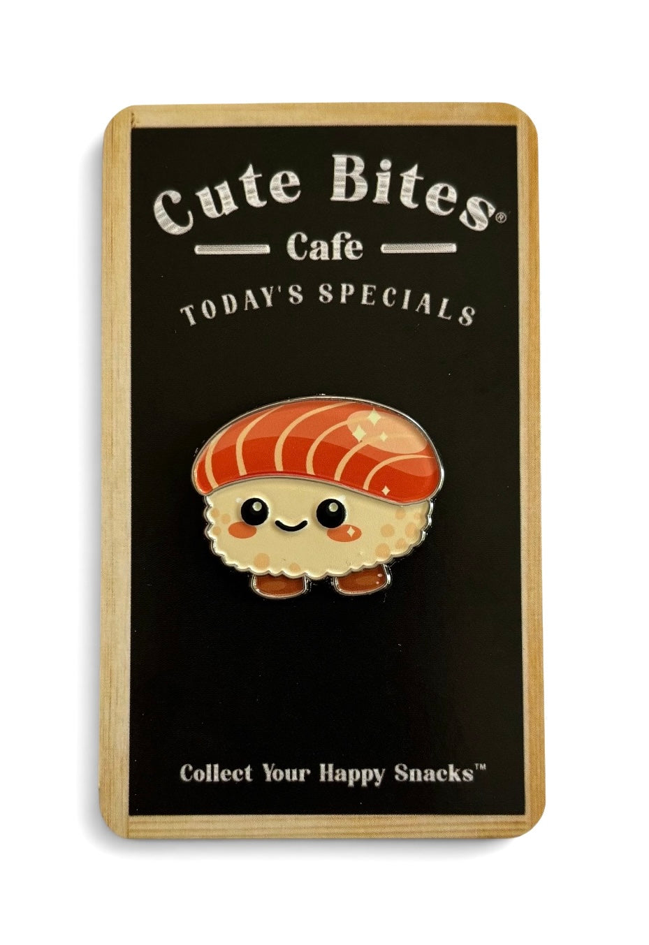 Enamel pin shaped like a cute, sweet salmon sushi snack, mounted on a black display card with 'Cute Bites Cafe' branding and a light wood border.