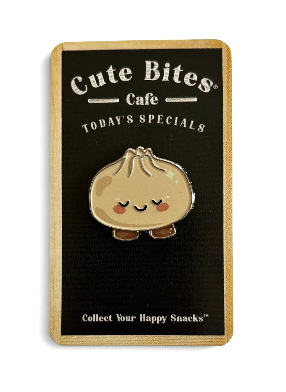 A cute kind dumpling shaped enamel pin displayed on a black and light wood backing card from Cute Bites Cafe.